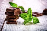 A few cubes of black chocolate with mint leaves on wooden table  Obrazy do Kuchni  Obraz