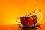 Tea splashing out of glass with orange background  Obrazy do Jadalni Obraz