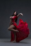 Young beautiful exotic eastern women performs belly dance in ethnic red dress on gray background Fototapety do Szkoły Tańca Fototapeta
