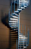 Metal spiral staircase casting shadow on wall in evening light  Schody Fototapeta