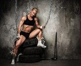 Beautiful muscular bodybuilder woman sitting on tyres  Fototapety do Siłowni Fototapeta