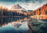 Lake with reflection in mountains at sunrise in autumn in Dolomites, Italy. Landscape with Antorno lake, small wooden bridge, trees with orange leaves, high rocks, blue sky in fall. Colorful forest Krajobraz Fototapeta