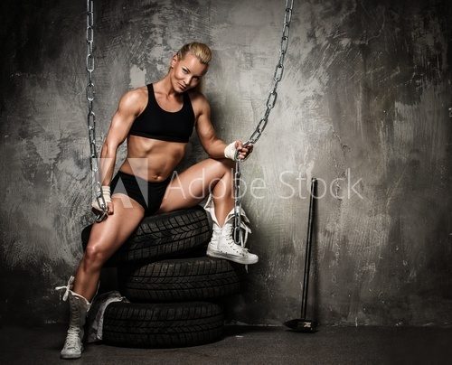 Beautiful muscular bodybuilder woman sitting on tyres  Fototapety do Siłowni Fototapeta