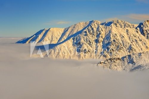 Ośnieżone górskie szczyty wynurzające się z mgły Fototapety Góry Fototapeta