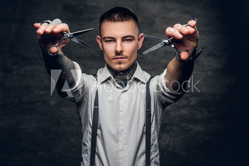 Portrait of tattooed male barber holds sharp scissors and a blade. Fototapety do Salonu Fryzjerskiego Fototapeta